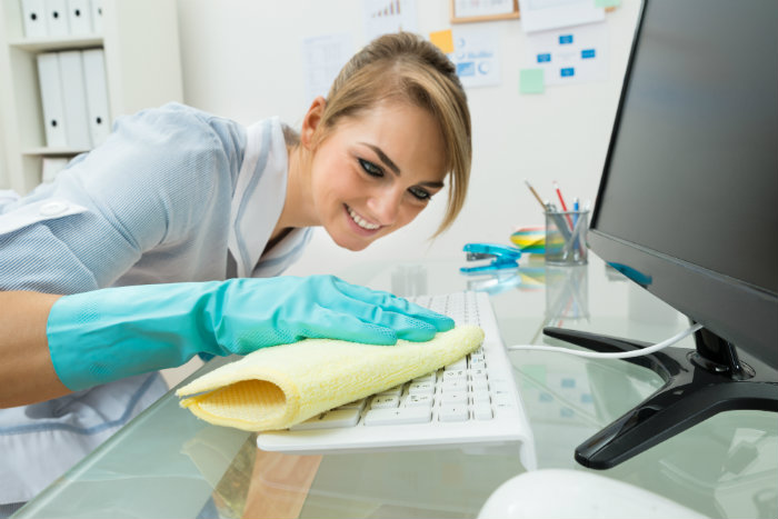 young woman wiping keyboard in office
