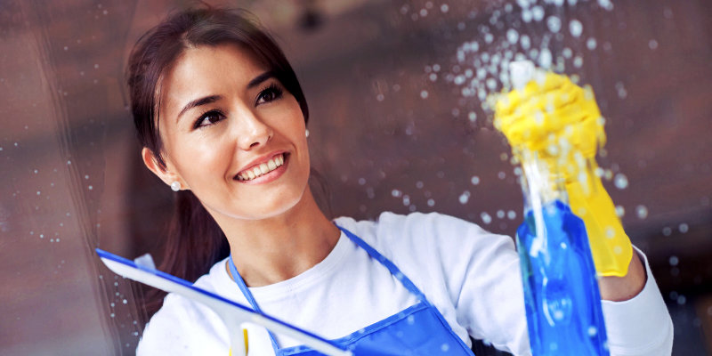 smiling young woman spraying solution on glass and wiping with squeegee