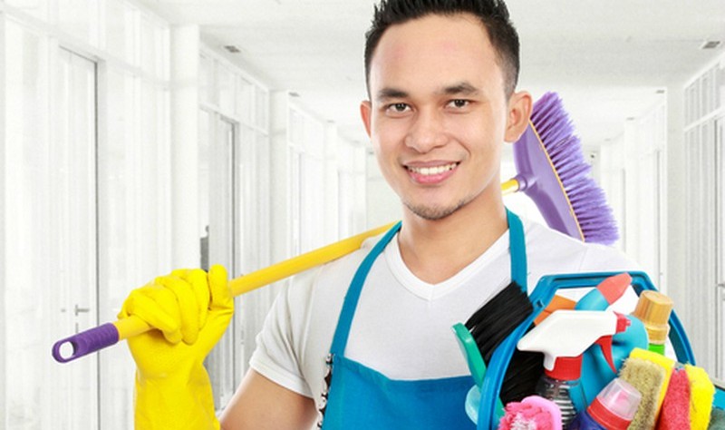 young man holding a bucket full of spray bottles and a broom in other hand