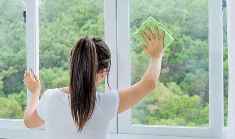 young woman wiping the window glass with a cloth rag