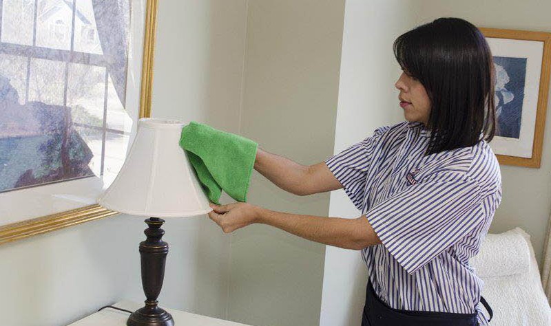 young woman wiping a table lamp with a cloth