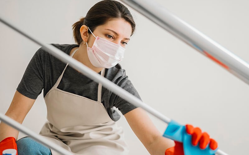 young woman wearing a mask wiping a grill