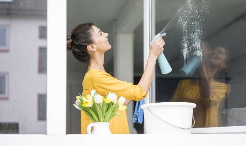 young woman spraying something on a window glass