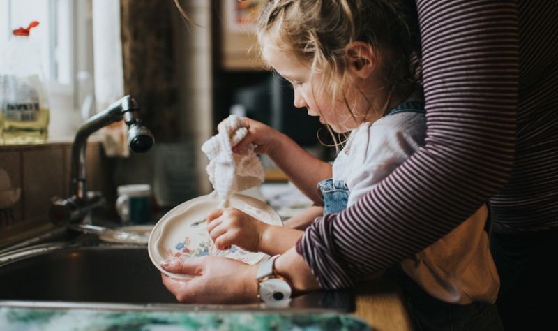 a mother teaching a kid how to do the dishes