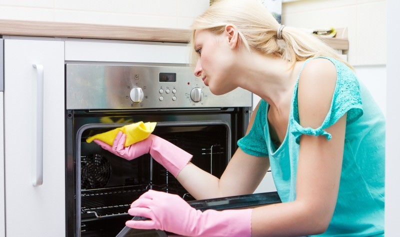 Young woman wiping a oven with a cloth rag