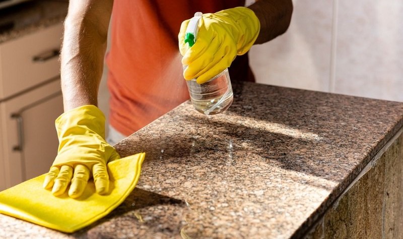 cropped picture of a person disinfecting granite surface