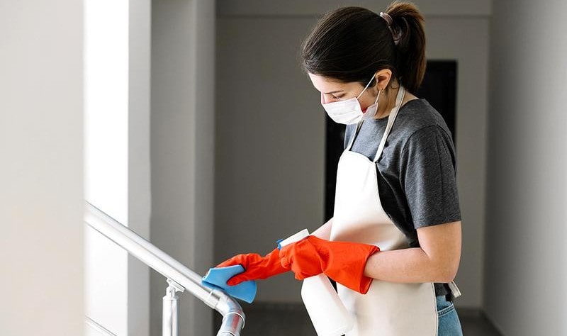 young woman wearing a mask disinfecting a surface