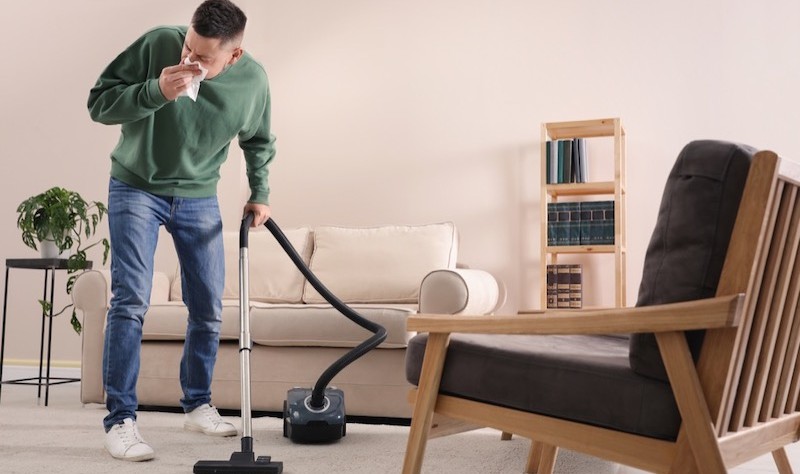 young man suffering from allergies and vacuuming the house