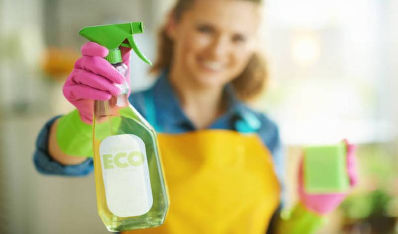 Woman holding green bottle and green scrubber in her hand