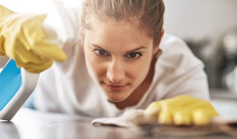 Woman in yellow gloves holding spray bottle in her hand spraying on a table