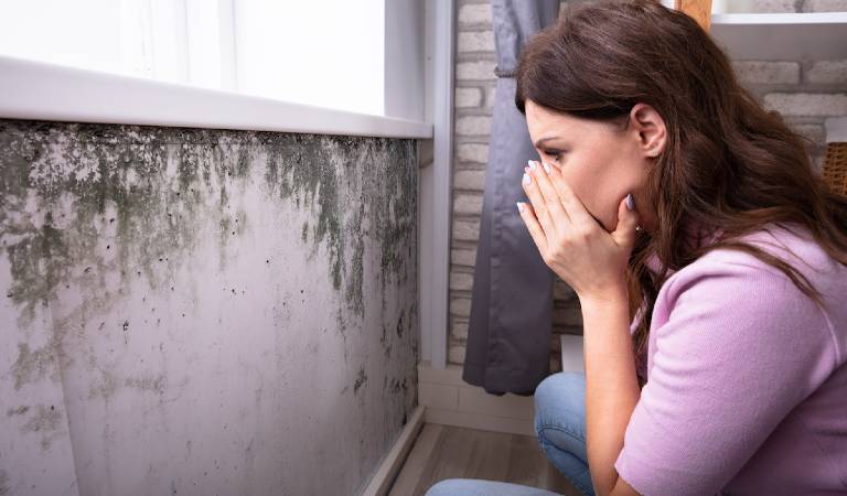 Woman in pink top is closing her mouth after seeing mold on walls