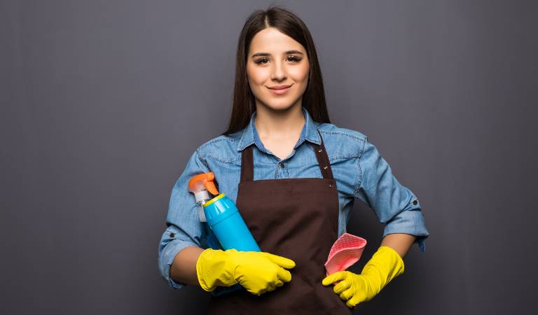 Woman in yellow gloves stand with blue bottle and cloth