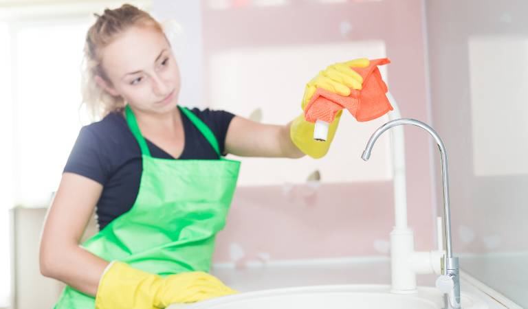Woman in black green dress and yellow gloves cleaning water tap