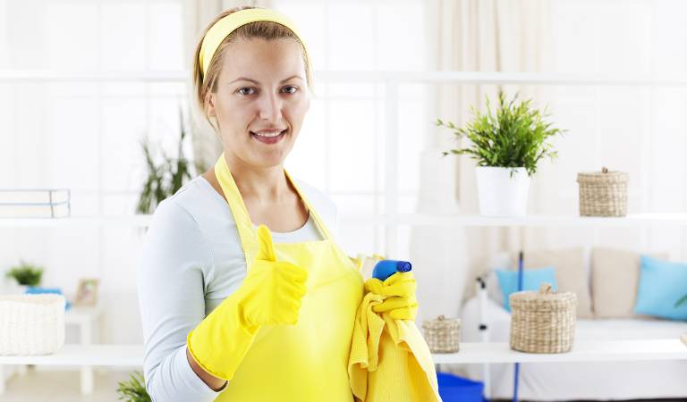 Woman in yellow gloves holding a bottle in her hand and thumps up.