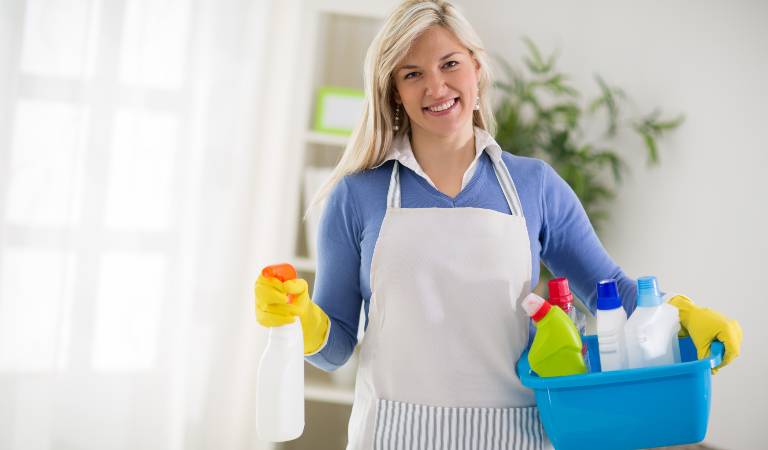 Woman holding a white bottle in one hand and a blue basket filled with tools in second hand
