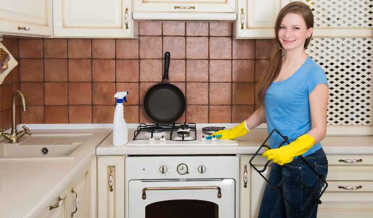 Woman in blue top, black jeans and yellow gloves standing in her kitchen