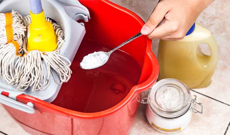 Hand of a woman preparing homemade cleaning product in a red basket using baking soda