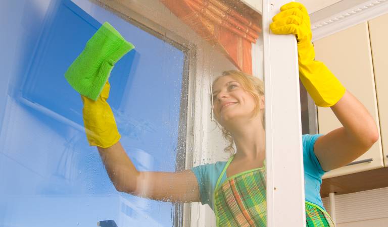 Woman in green top and yellow gloves cleaning window using a green cloth.