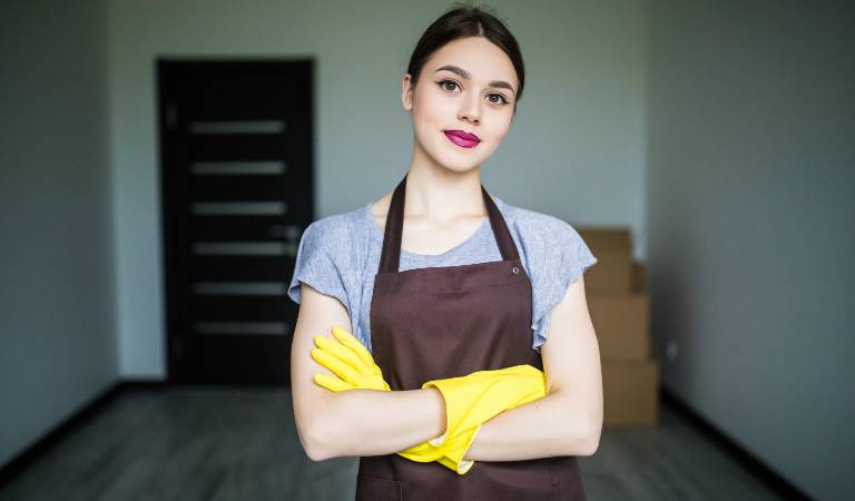 Woman in uniform and yellow glove inside a living room with some boxes behind her.
