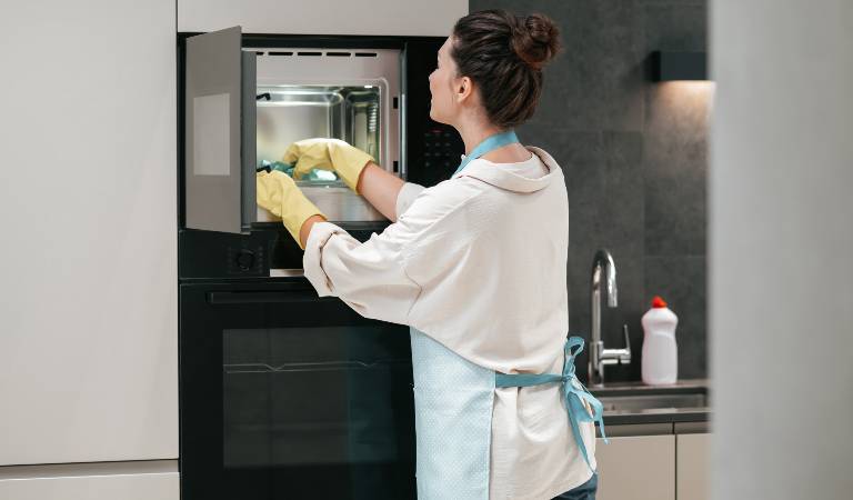 Woman in yellow gloves cleaning oven insider her kitchen.