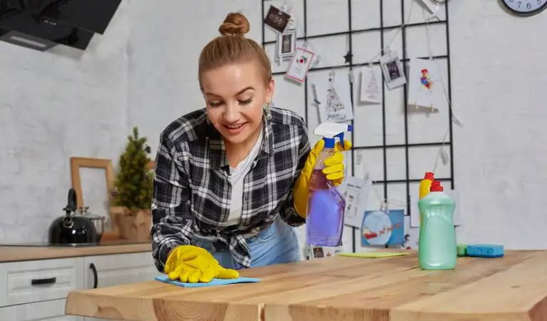 Lady in check shirt and yellow gloves cleaning a table