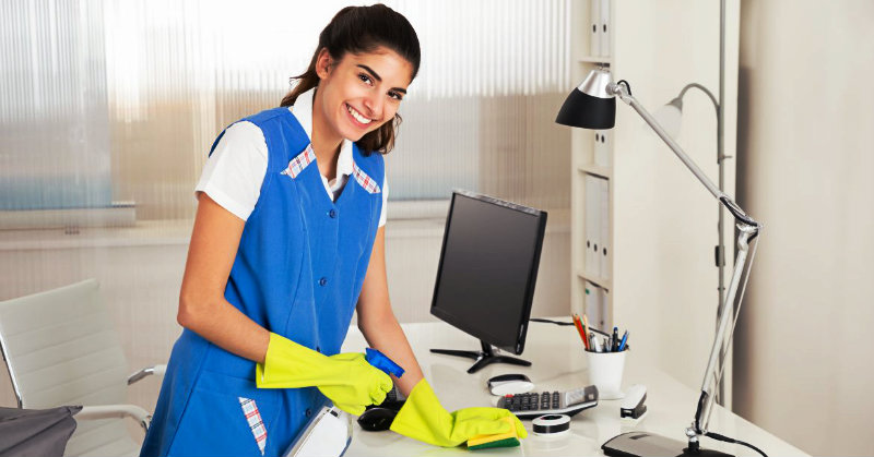 beautiful young woman happily wiping office table with sponge