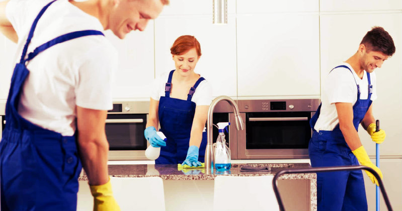Two men ans one womn in blue apron wiping and mopping kitchen