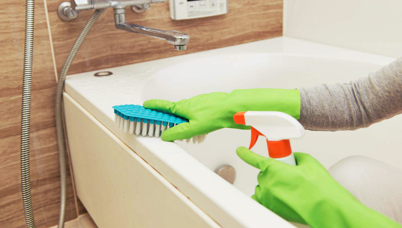 cropped image of a woman wiping bathtub with a brush