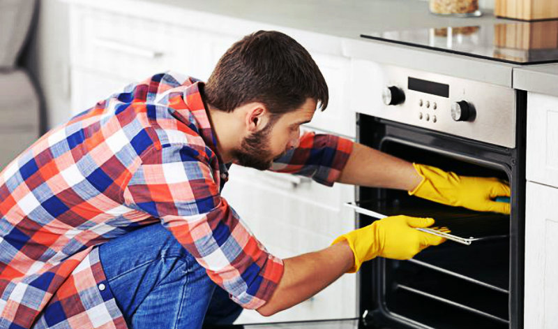 Young Man wearing protective gloves scrubbing the oven