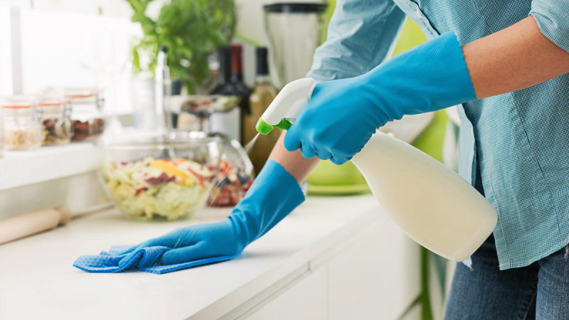 cropped image of a man wiping kitchen counter with scrub and spray bottle in hand