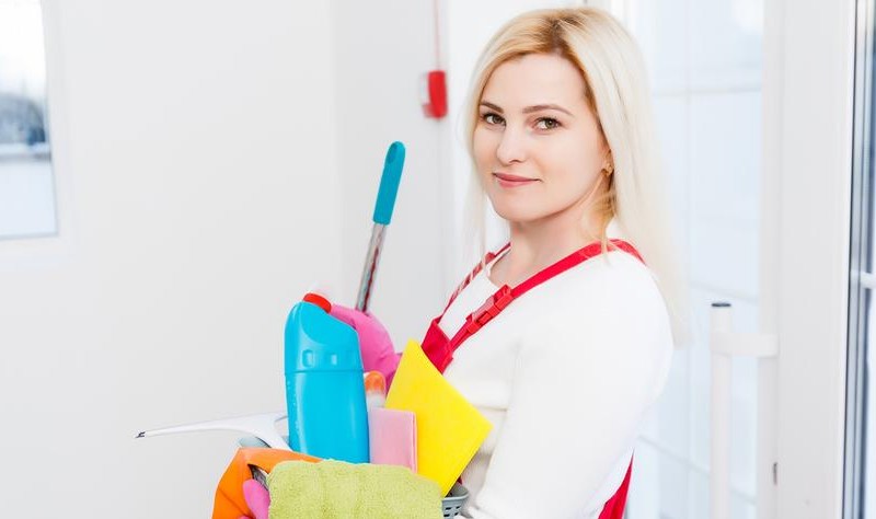 young woman holding a bucket full of chemical bottles and cloth wipes