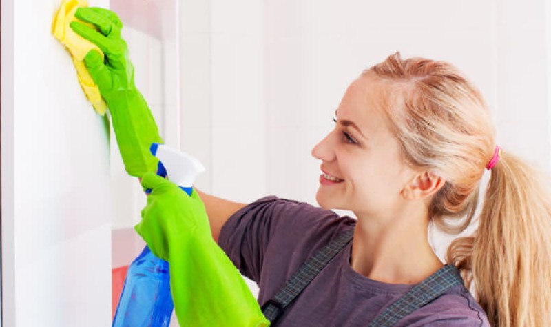 young woman with a spray bottle and cloth rag disinfecting a surface