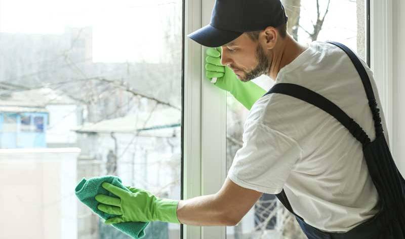 Men in blue cap and green gloves scrubbing window