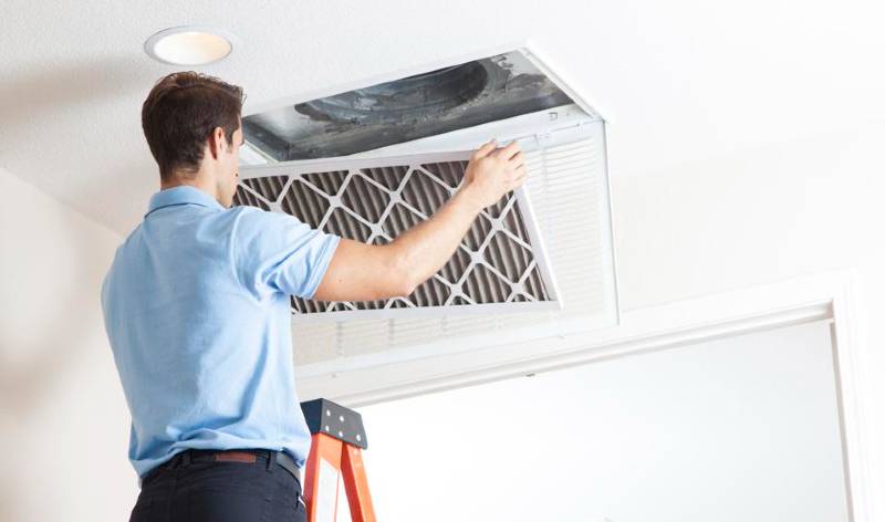 A man in blue t-shirt and black jeans opening air duct from ceiling
