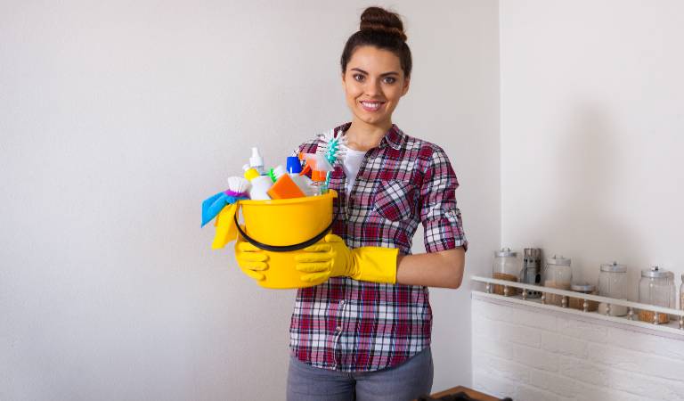 Woman in check shirt holding yellow basket with tools and supplies