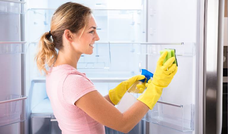 Woman in pink top and yellow gloves cleaning a fridge