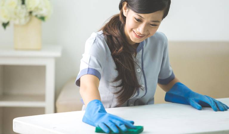 Woman in blue gloves scrubbing a table and smiling