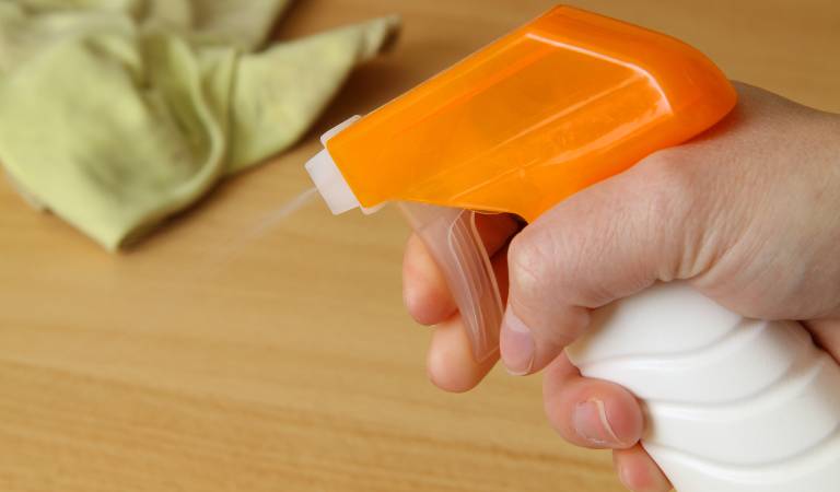 hand of a woman holding a white spray bottle with orange cap.