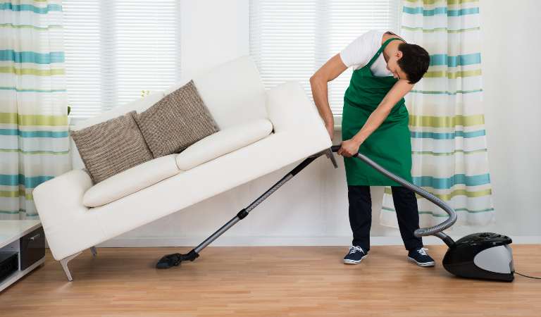 Full length man cleaning floor with with vacuum cleaner at home