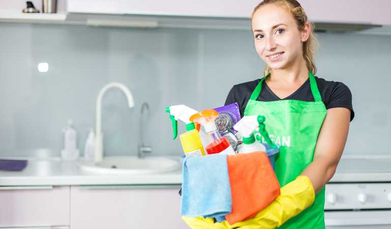 Woman in uniform and yellow glove holding a basket filled with tools, products, equipment.