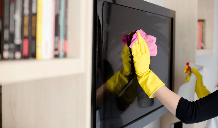 Hand of a woman in black top and yellow gloves cleaning tv screen.