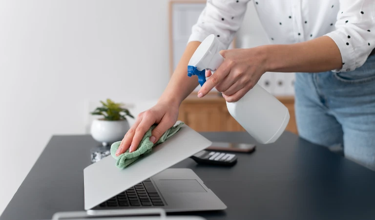 Woman holding a white spray bottle cleaning her laptop
