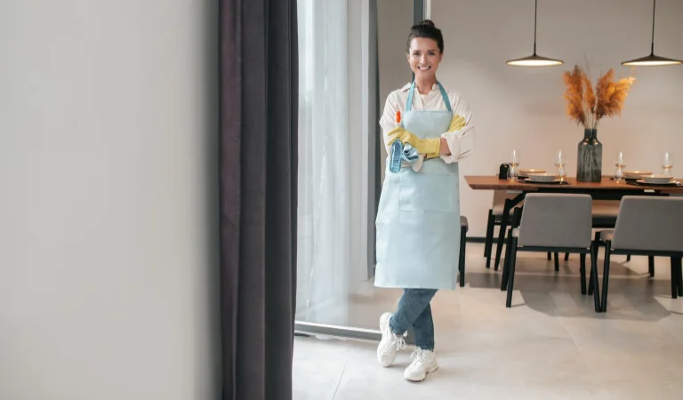 A lady in yellow gloves holding a bottle in her hand inside a living room.